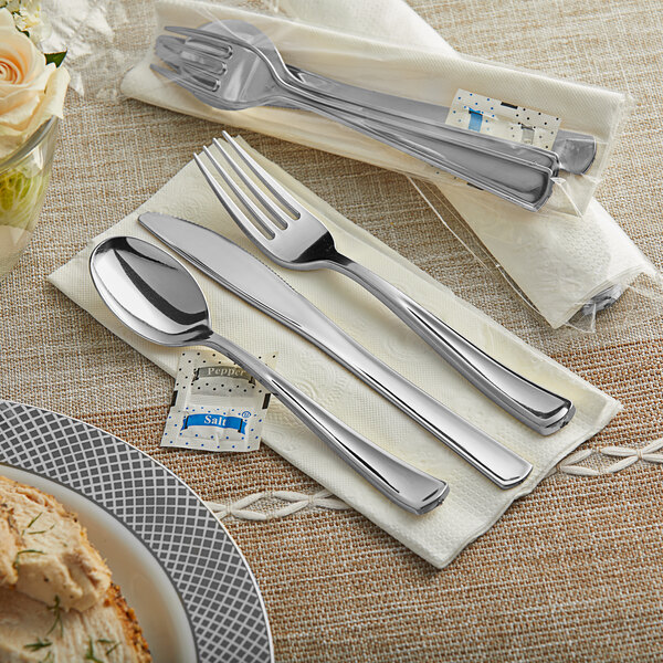 A Visions silver plastic cutlery set on a napkin next to a plate of food.