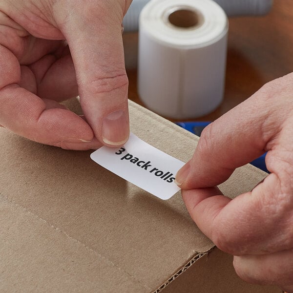 A person's hand using a Lavex white direct thermal label with black text to label a box.