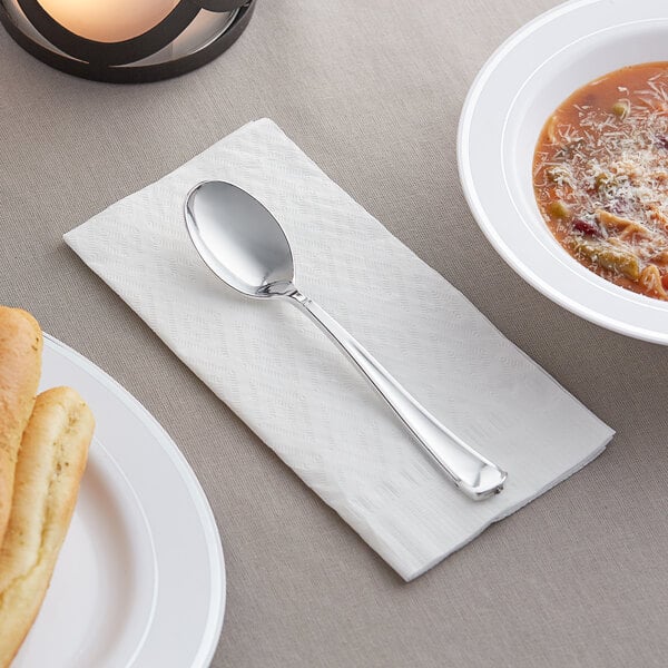 A Visions silver plastic spoon on a napkin next to a bowl of soup.