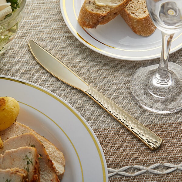 A Visions Hammersmith gold plastic knife on a plate of food and a glass of water.