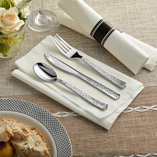 A Visions pre-rolled napkin with Hammersmith silver plastic cutlery on a napkin next to a plate of food.