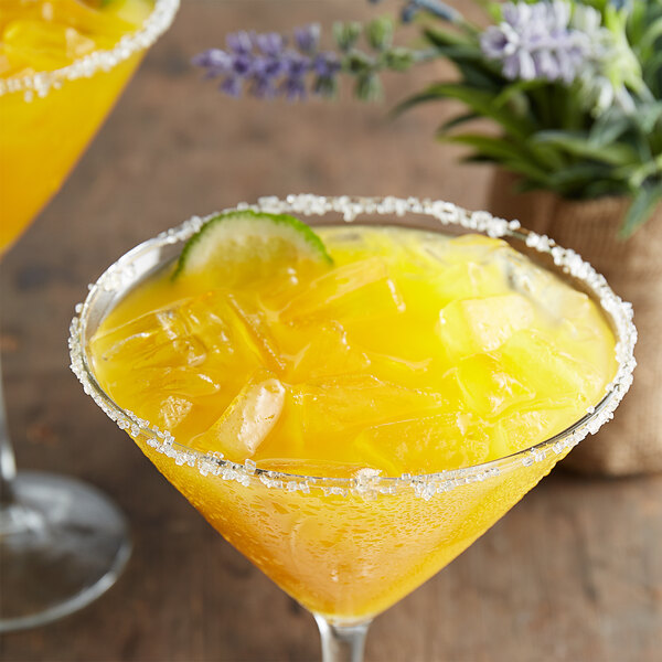 A yellow drink with ice and lime made with Les Vergers Boiron Mango Puree in a martini glass.
