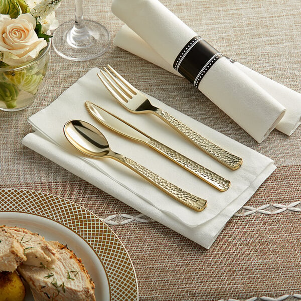 A table setting with a Visions pre-rolled napkin, gold plastic fork, knife, and spoon on a plate of food.
