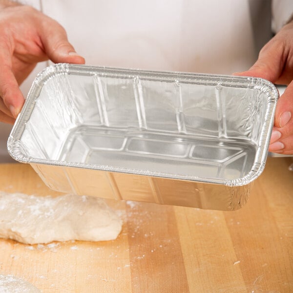 A person pouring dough into a D&W aluminum foil loaf pan.