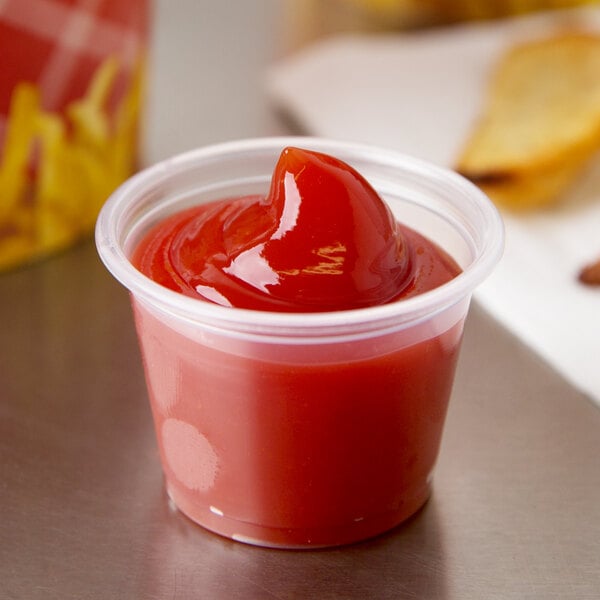 A Dart plastic souffle container filled with red ketchup on a table.