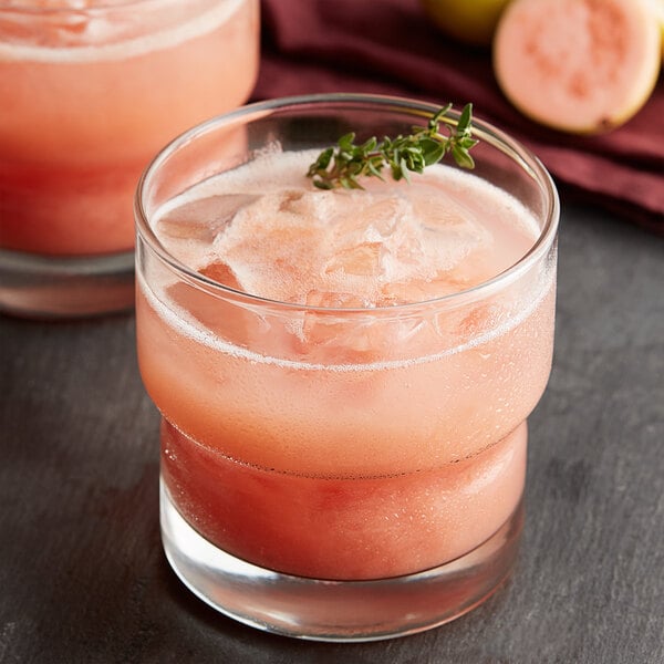 A glass of pink drink with Les Vergers Boiron Pink Guava Puree and ice, garnished with a sprig of thyme.