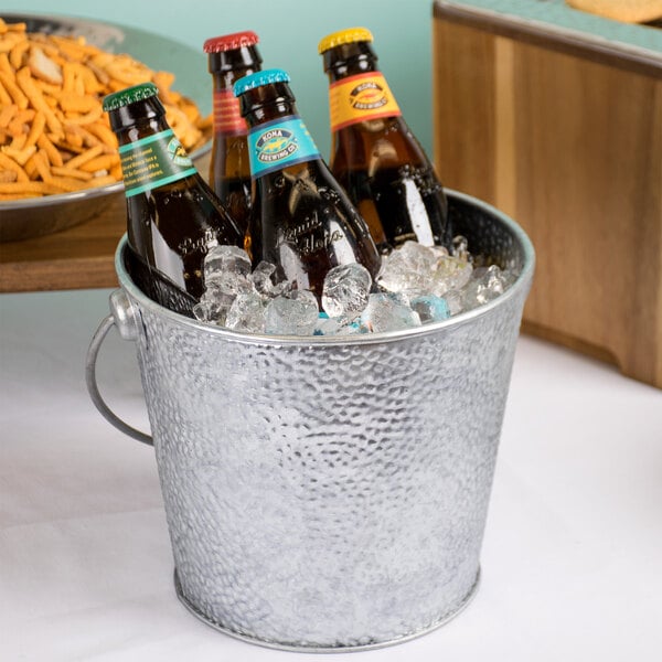 A Tablecraft galvanized steel beverage bucket filled with ice and bottles of beer.