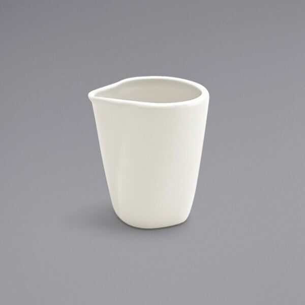 A Front of the House European white porcelain creamer with a curved top on a white background.