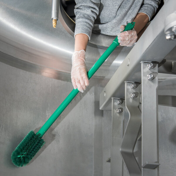 A person in gloves cleaning a stainless steel tank with a Carlisle green brush with a green handle.