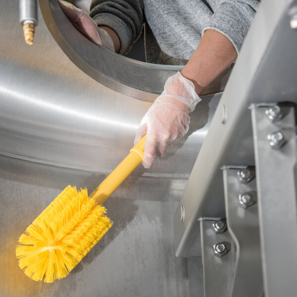 A person wearing gloves cleaning with a yellow Carlisle Sparta brush.