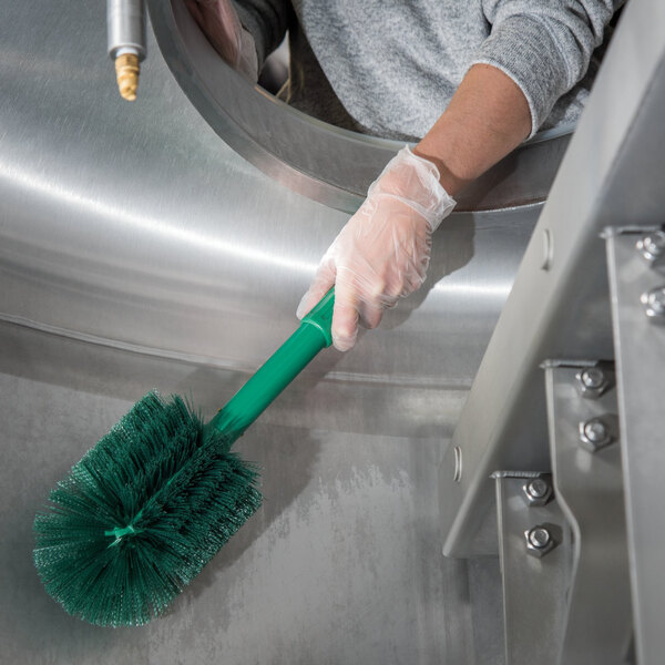 A hand holding a green Carlisle Sparta multi-purpose cleaning brush.