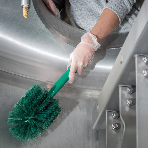 A person in gloves cleaning a metal sink with a Carlisle green Sparta brush.