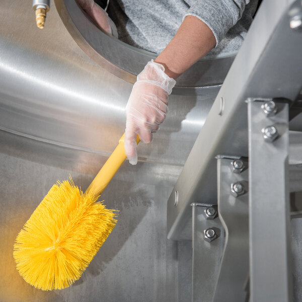 A person wearing gloves and using a Carlisle yellow brush to clean.