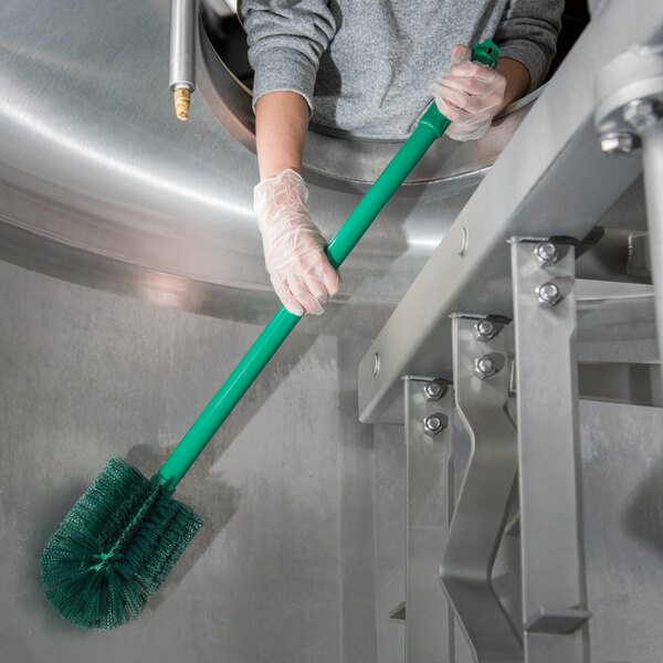 A person holding a Carlisle green Sparta multi-purpose cleaning brush with a green handle.