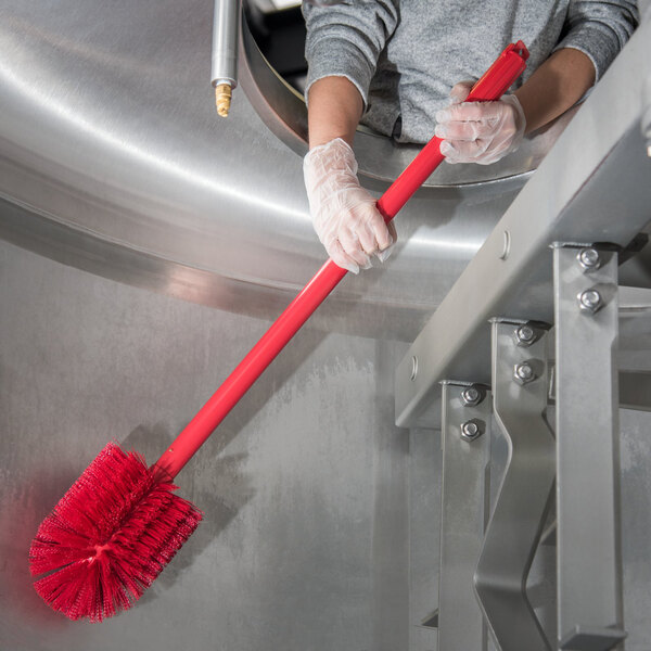 A person in gloves using a Carlisle red multi-purpose cleaning brush with a red tube.