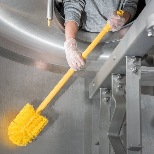 A person in gloves using a Carlisle yellow brush with a yellow handle to clean a metal container.