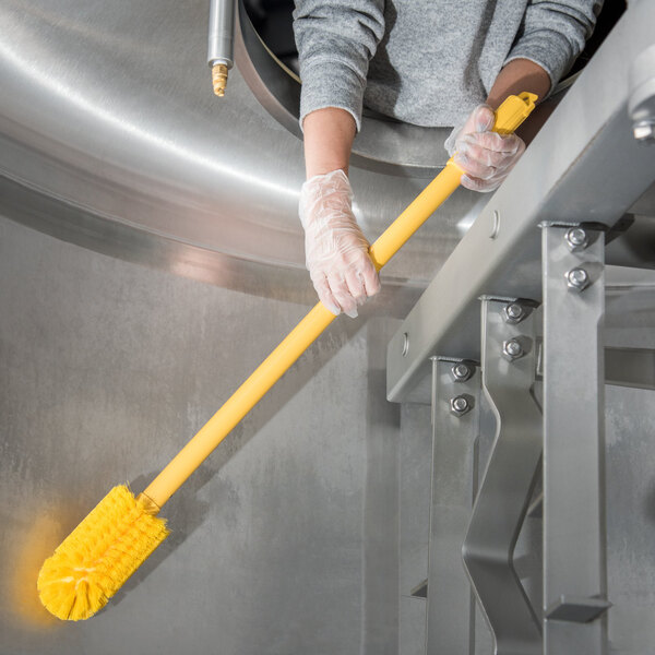 A person in gloves using a Carlisle yellow multi-purpose brush to clean.