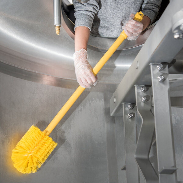 A person in gloves using a Carlisle yellow Sparta multi-purpose brush to clean.