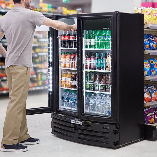 A man looking at a Beverage-Air refrigerated glass door merchandiser filled with drinks.