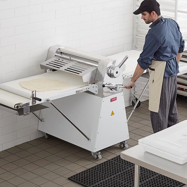 A man in an apron and gloves using an Estella dough sheeter to roll out dough.