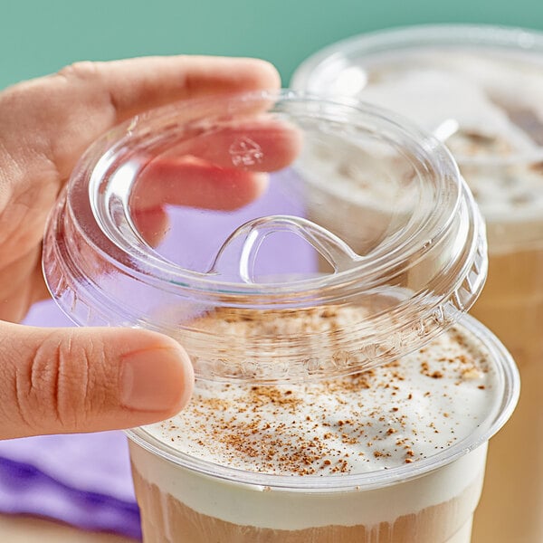 A hand putting a Choice clear plastic sip-through lid on a cup of coffee.