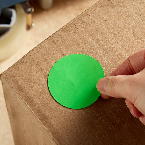 A hand putting a Lavex fluorescent green circle label on a cardboard box.