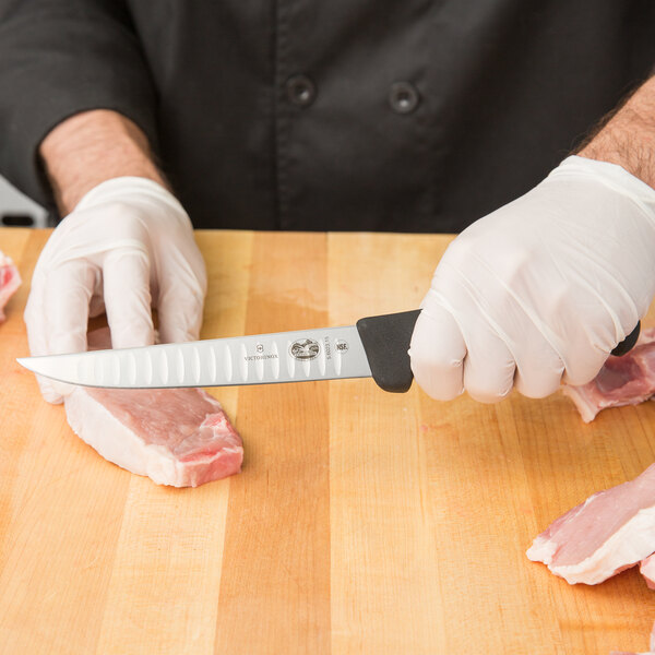 A person in a white glove using a Victorinox boning knife to cut meat on a cutting board.