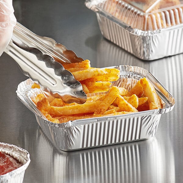 A person using tongs to serve french fries in a Choice oblong foil container.