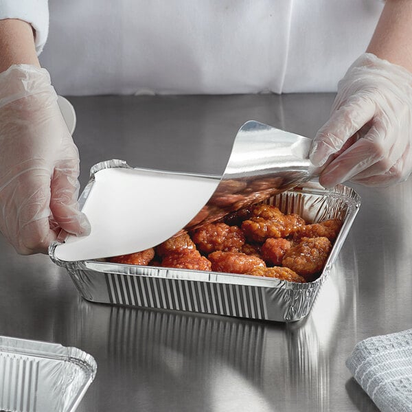 A person in gloves holding a Choice foil laminated board lid filled with food.