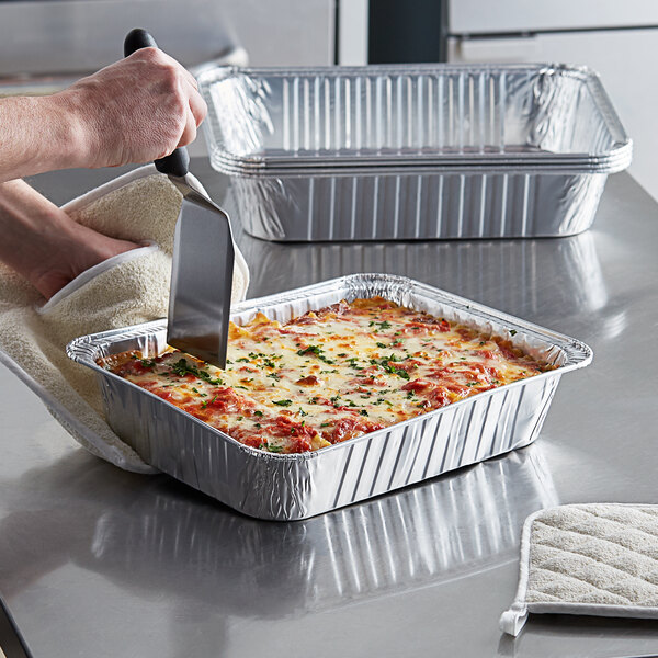 A person using a spatula to serve food from a Choice rectangular foil pan.