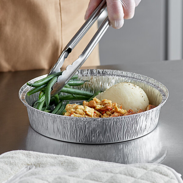A person using tongs to serve food from a Choice tin pan.