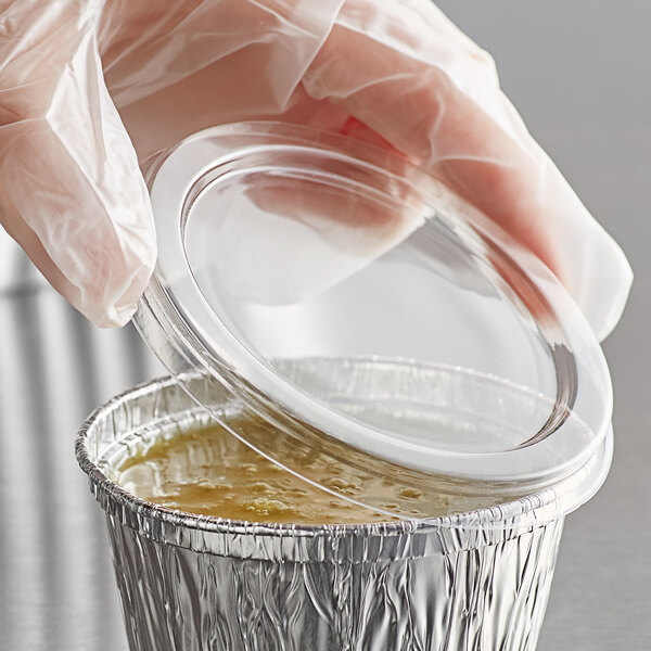 A gloved hand placing a plastic lid on a small clear plastic container.