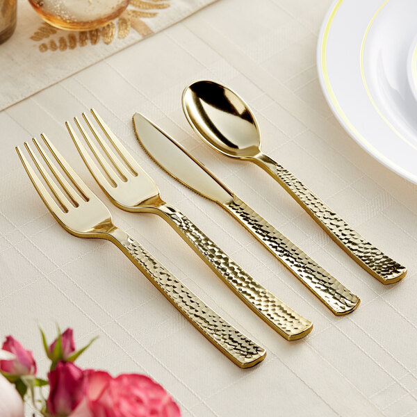 A Visions Hammersmith gold plastic cutlery set with gold forks and knives on a table.