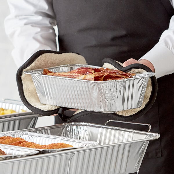 A person holding a Choice foil steam pan filled with food.