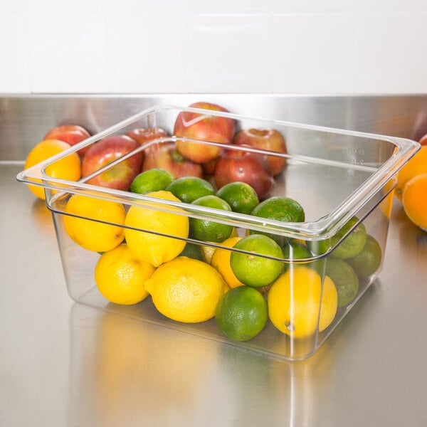 A Cambro clear plastic food pan filled with lemons and oranges on a counter.