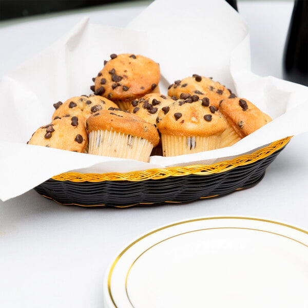 A Thunder Group oval rattan bread basket filled with muffins on a table.