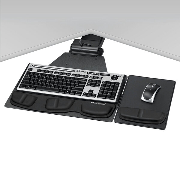 A Fellowes black and silver keyboard and mouse on a Fellowes keyboard tray under a white desk.