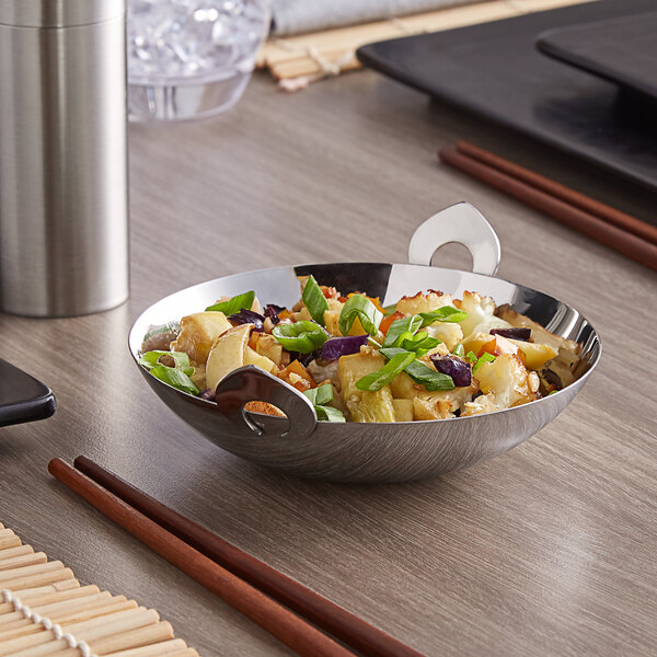 A mini stainless steel wok with food and chopsticks in it on a table.