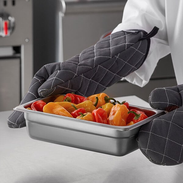 A chef holding a Carlisle stainless steel hotel pan full of peppers.
