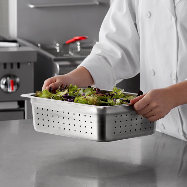 A chef holding a Carlisle stainless steel hotel pan with salad inside.