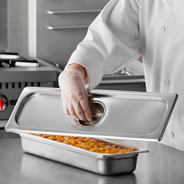 A person wearing gloves is putting macaroni into a Carlisle stainless steel steam table pan.