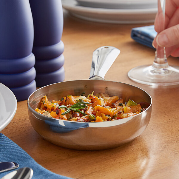 A Vollrath mini stainless steel fry pan with food on a table.