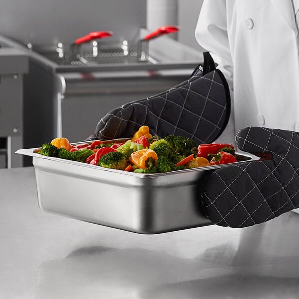 A chef holding a Carlisle stainless steel steam table pan full of broccoli and carrots.