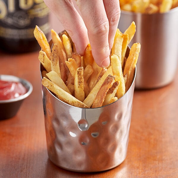 A hand holding a cup of french fries with a french fry in it.