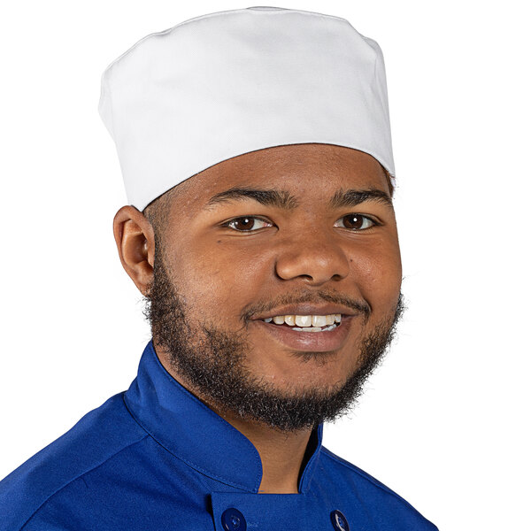 A smiling black man wearing a white Uncommon Chef skull cap in a professional kitchen.