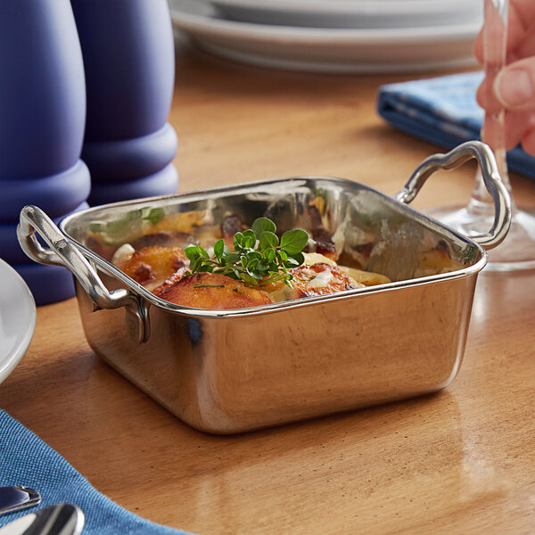 A silver Vollrath square mini roasting dish with food in it and handles.