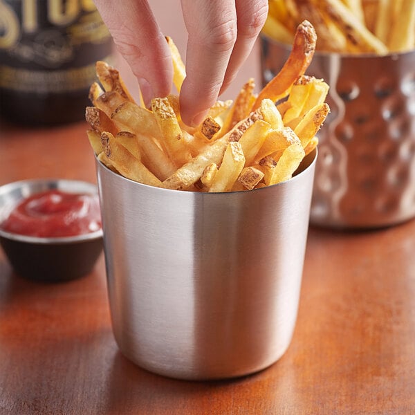 A person's hand taking french fries out of a Vollrath stainless steel cup.
