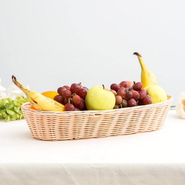 A beige woven rattan bread basket filled with fruit on a table.