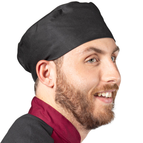 A man wearing a black Uncommon Chef skull cap at a deli counter.