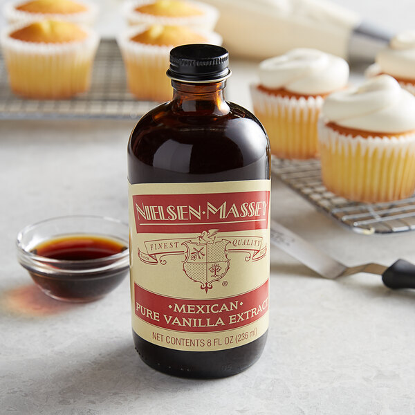 A bottle of Nielsen-Massey Mexican Vanilla Extract next to cupcakes.